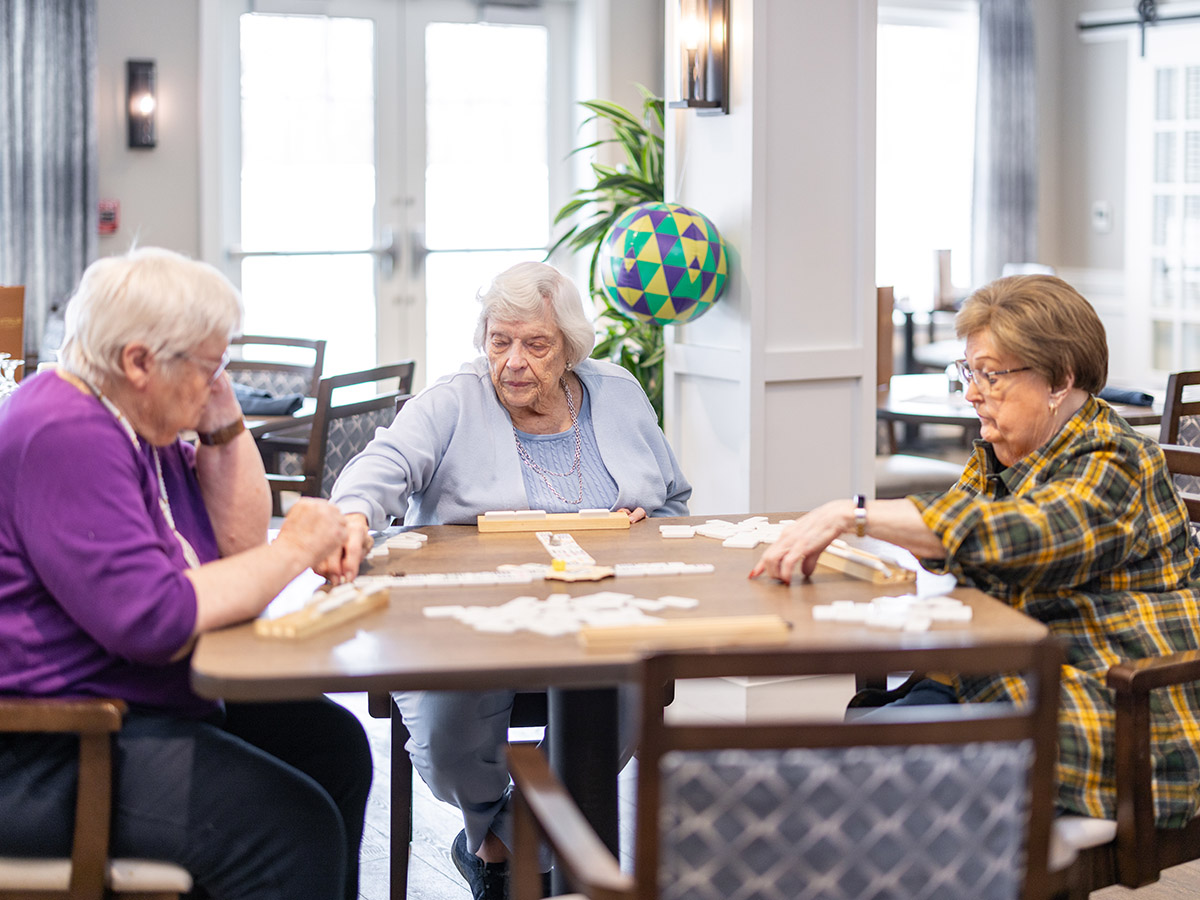 Three elderly women residents playing a game of dominos at a table.