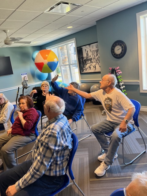 Fun chair volleyball game with a beachball at an employee beachball orientation for senior living residents.