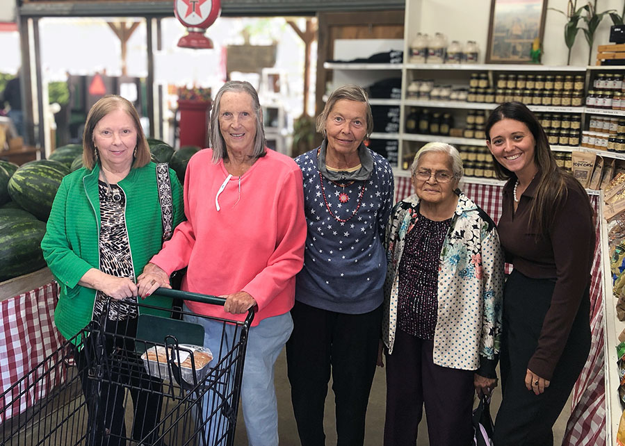 Team members and residents smile while out a local shop, surrounded by fresh jams and produce.