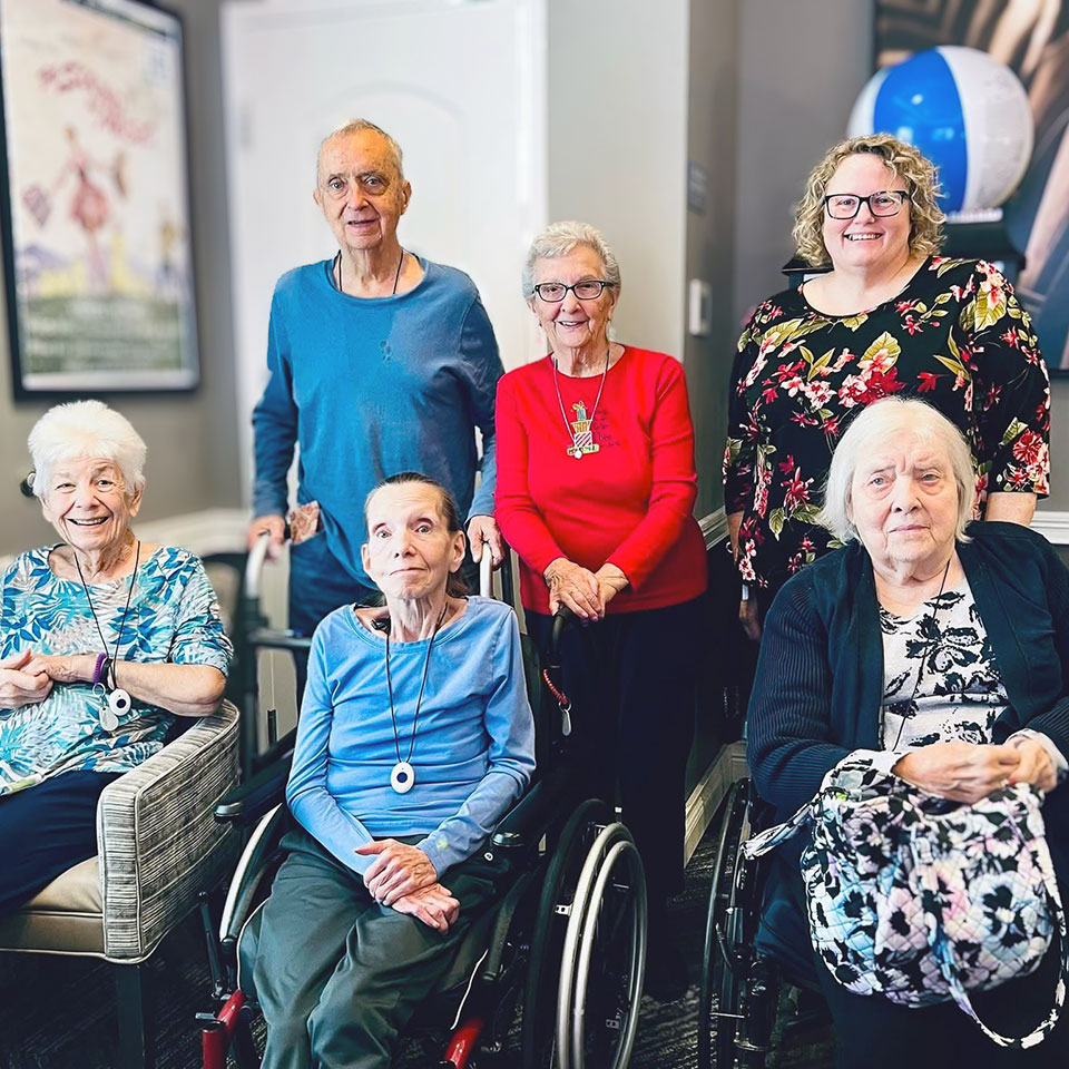 A group of senior residents and friends gather in the fitness room, smiling.