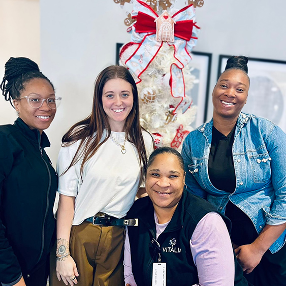 Four women on the Vitalia Montrose team smile proudly in front of a themed tree at the community.